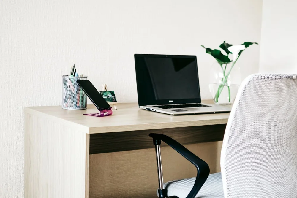 A simple workspace with a laptop, phone and plant on a wooden desk
